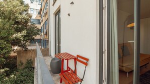 Un balcón con un banco rojo y una maceta grande, con vista a un paisaje urbano.