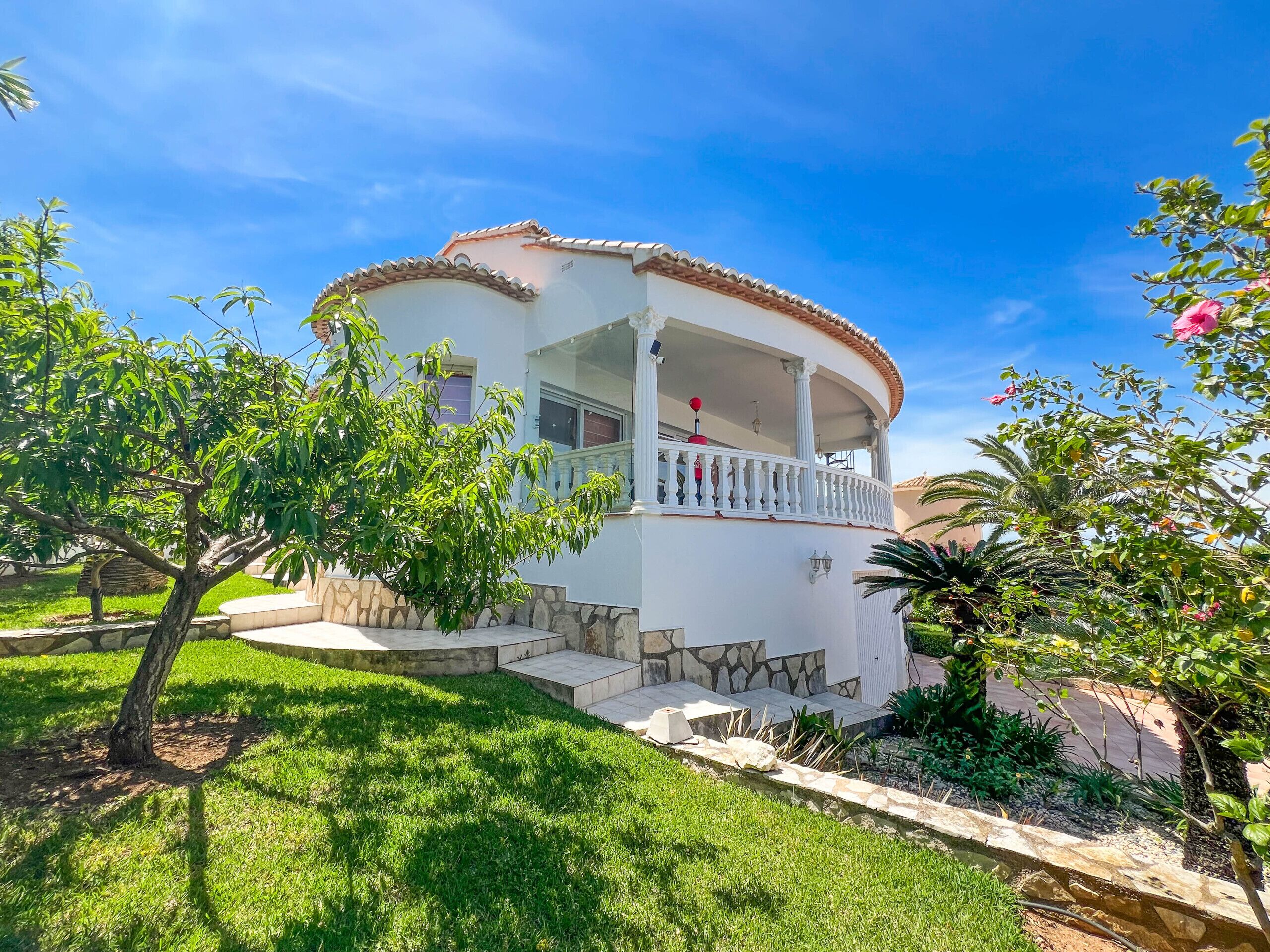 A two-story house with a balcony, surrounded by well-maintained grass and trees.