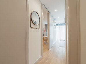 Ein Flur mit einem runden Spiegel an der Wand, einer Tür zu einem Raum mit Tisch und Stühlen sowie einem Fenster mit Vorhängen.