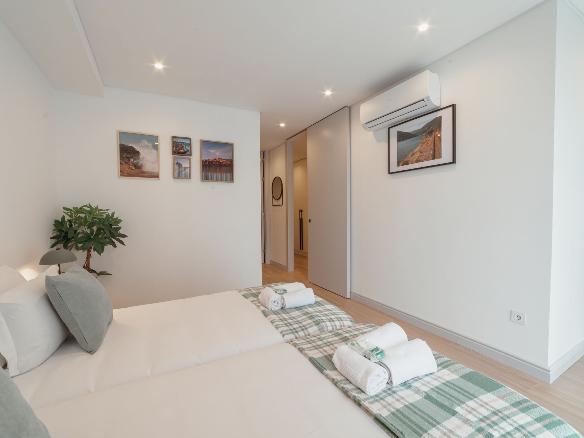 A modern bedroom with a bed, a plant, and a wall-mounted air conditioner.