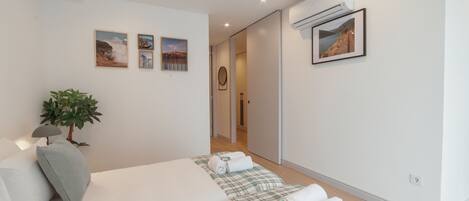 A modern bedroom with a bed, a plant, and a wall-mounted air conditioner.