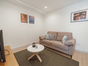 Ein modernes Wohnzimmer mit einem beigefarbenen Sofa, einem kleinen runden Tisch und zwei gerahmten Kunstwerken an der Wand.