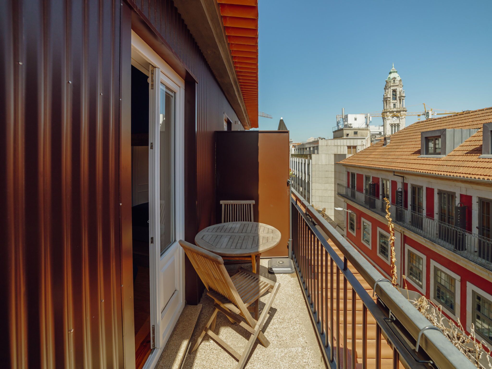 Un balcon avec une table et des chaises, une vue sur un paysage urbain avec des immeubles et un ciel dégagé.