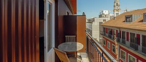 A balcony with a table and chairs, a view of a cityscape with buildings, and a clear sky.