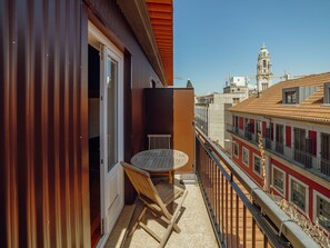 Ein Balkon mit Tisch und Stühlen, Blick auf eine Stadtlandschaft mit Gebäuden und einem klaren Himmel.