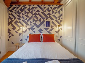 Ein Zimmer mit einem Bett, zwei Kissen, einem Nachttisch und einer Wand mit geometrischem Muster.
