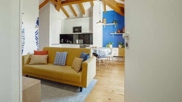 Ein modernes Wohnzimmer mit Sofa, einem Esstisch mit Stühlen, einer Küchenzeile mit Geräten und einer blauen Akzentwand.