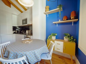 Eine kompakte Küche mit modernen Geräten, ein Essbereich mit gemustertem Tischlein und eine blaue Wand mit dekorativen Regalen.