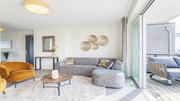 Uma sala de estar moderna com um sofá seccional, uma mesa de centro redonda e uma janela grande.