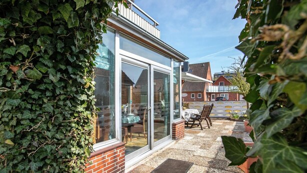 Een terras met een tafel, stoelen, een glazen deur en een met klimop begroeide muur.
