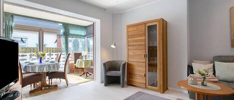A modern living room with a dining area, a grey armchair, a wooden cabinet, and a round table with a vase.