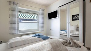 Een slaapkamer met twee bedden, een televisie en een schuifdeur naar een badkamer.