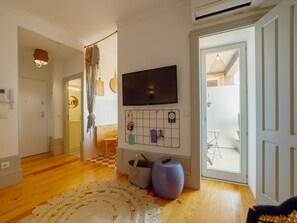 A modern living room with a flat-screen TV mounted on the wall, a wooden floor, a patterned rug, and a large window. - Apartment  by Interhome (Porto)