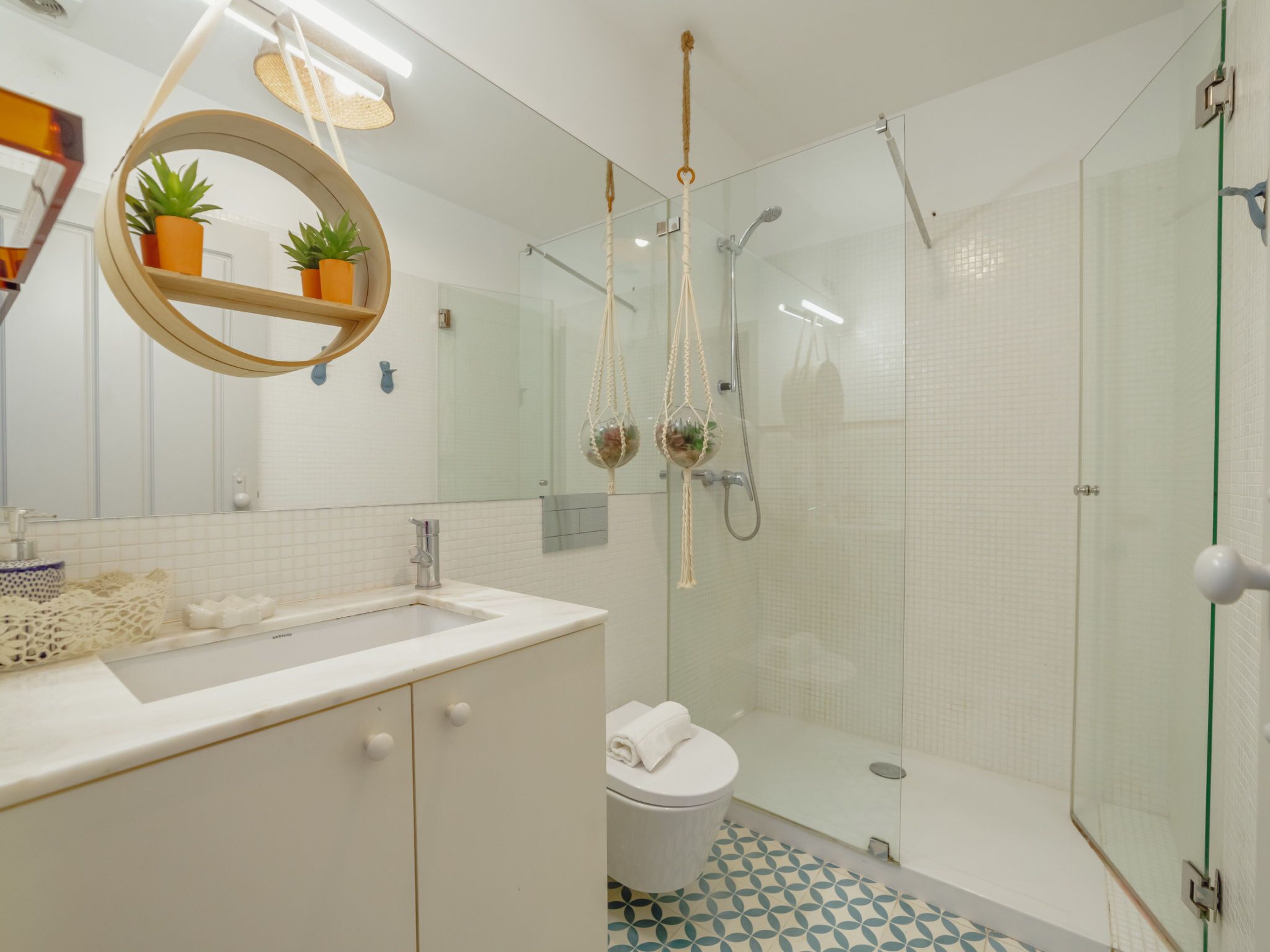 Un bagno moderno con cabina doccia in vetro, uno specchio tondo con una pianta e un lavandino bianco.