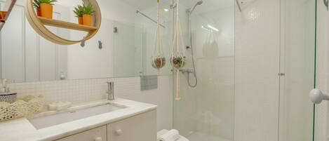Un bagno moderno con cabina doccia in vetro, uno specchio tondo con una pianta e un lavandino bianco.