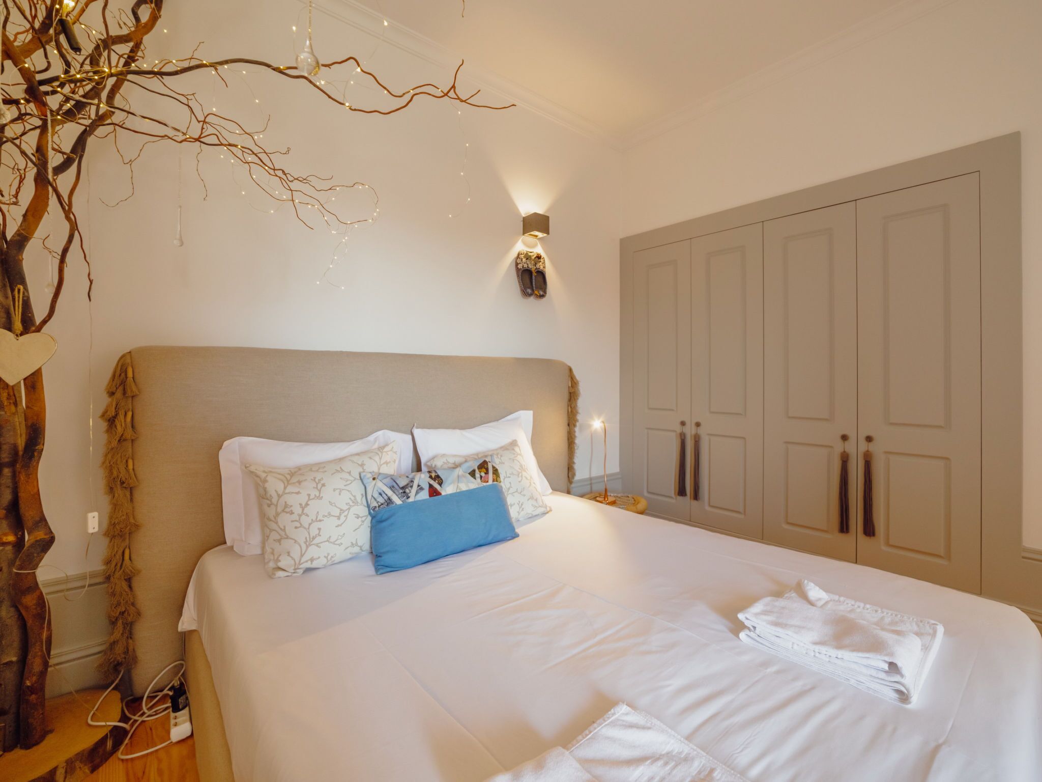 Een netjes opgemaakt bed met witte lakens en een blauw kussen, een wandlamp en een grote inbouwkast met deuren.