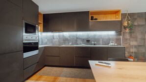 Uma cozinha moderna com armários escuros, forno de aço inoxidável, micro-ondas embutido e bancada de madeira.
