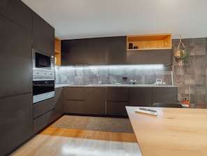 Eine moderne Küche mit dunklen Schränken, einem Edelstahlbackofen, einer eingebauten Mikrowelle und einer Holz Arbeitsplatte.