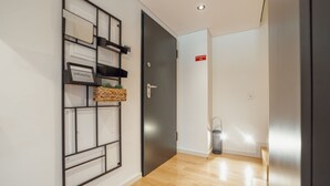 Um corredor com piso de madeira, uma porta preta e um prateleira fixada na parede com uma placa de boas-vindas.