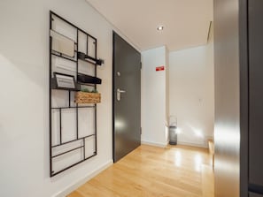 Ein Flur mit Holzboden, einer schwarzen Tür und einem an der Wand befestigten Regal mit einer Willkommensschild.