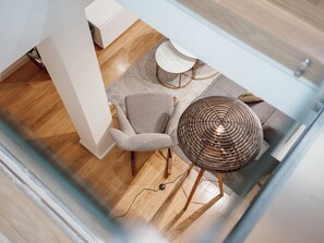 Ein modernes Interieur mit Holzboden, einem grauen Sessel, einem runden Tisch mit Geflechtfuß und einem weißen Stuhl.