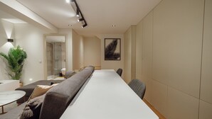 Um interior moderno com uma mesa branca comprida, sofás cinzas e uma planta grande.