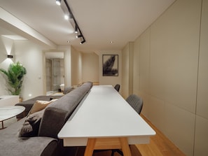 Ein modernes Interieur mit einem langen weißen Tisch, grauen Sofas und einer großen Pflanze.