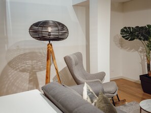Ein modernes Wohnzimmer mit einem grauen Sofa, einer Stehlampe mit Holzfuß und einer großen Topfpflanze.
