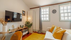 Una sala de estar moderna con televisor de pantalla plana, un sofá con cojines amarillos, una mesa de centro de madera y un ventanal con cortinas.