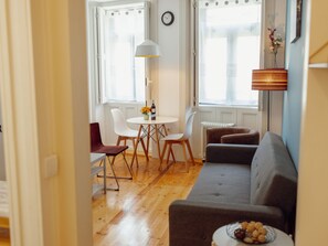 A living room with a sofa, a dining table with chairs, a lamp, and a clock on the wall. - Apartment  by Interhome (Porto)