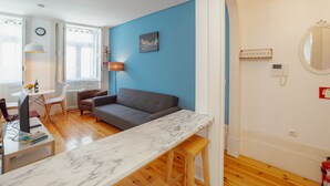 A modern living room with a blue accent wall, a grey sofa, a marble coffee table, and a dining area with a white table and chairs. - Apartment  by Interhome (Porto)