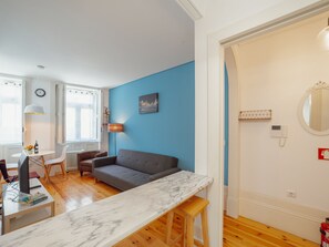 A modern living room with a blue accent wall, a grey sofa, a marble coffee table, and a dining area with a white table and chairs. - Apartment  by Interhome (Porto)