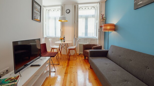 A modern living room with a flat-screen TV, a grey sofa, a dining table with chairs, and a large window with curtains. - Apartment  by Interhome (Porto)