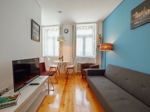 A modern living room with a flat-screen TV, a grey sofa, a dining table with chairs, and a large window with curtains. - Apartment  by Interhome (Porto)