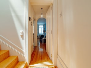 A hallway with wooden flooring, white walls, and a door leading to a room with a blue accent wall. - Apartment  by Interhome (Porto)