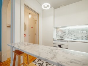 A modern kitchen with a marble countertop, wooden stools, and white cabinetry. - Apartment  by Interhome (Porto)