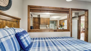Een slaapkamer met een bed, een grote spiegel, een houten hoofdbord en een uitzicht op de keuken via de spiegel.
