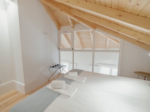 A bedroom with a sloped ceiling, a bed with white linens, a small table with a chair, and a window providing natural light. - Apartment  by Interhome (Porto)