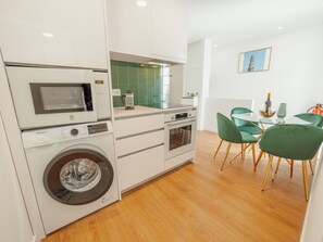 Une cuisine moderne équipée d’un lave-linge, d’un four à micro-ondes et d’un coin repas avec des chaises vertes.