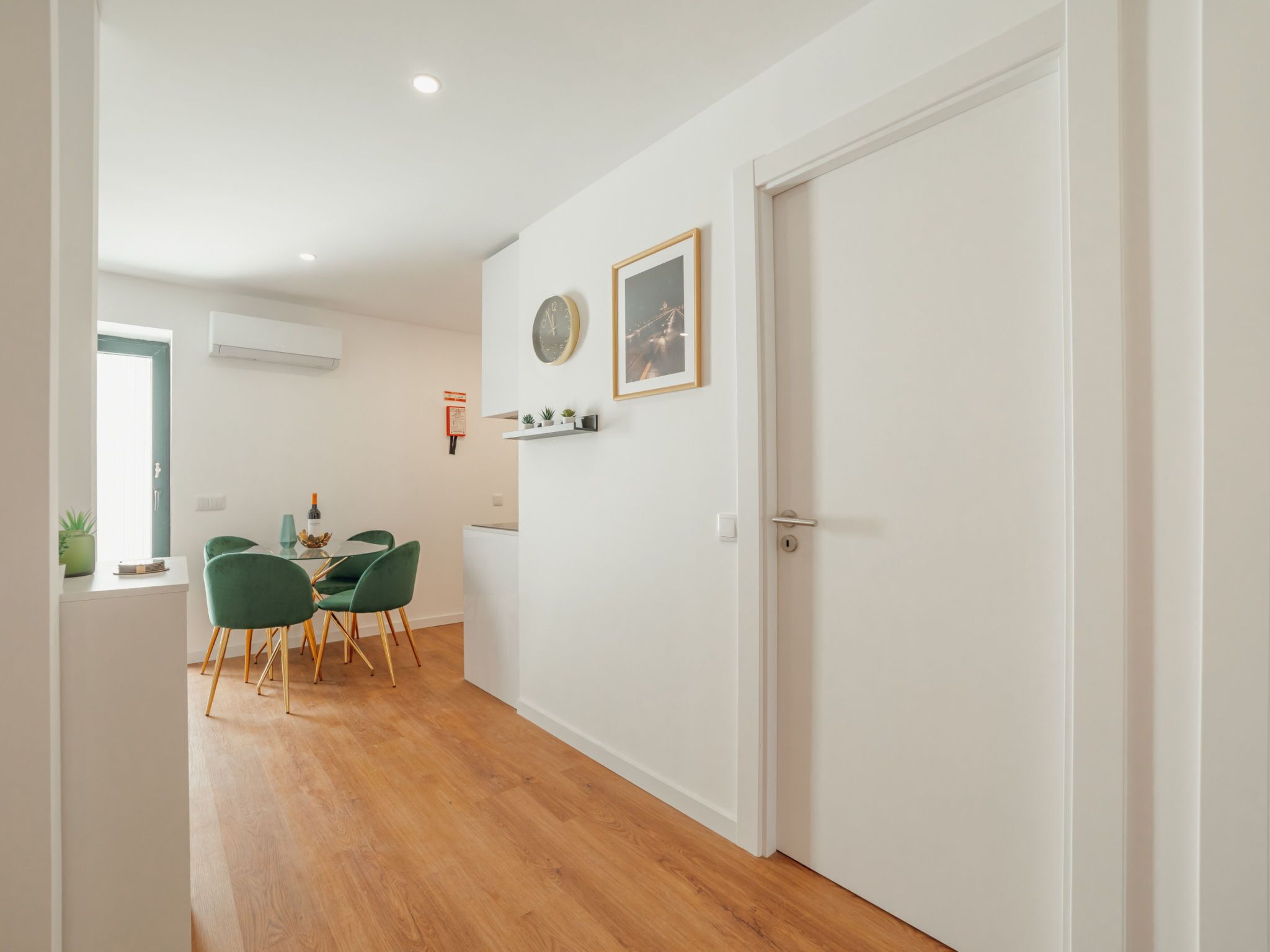 A hallway with a dining area featuring a table with chairs, a clock, and a framed picture on the wall.