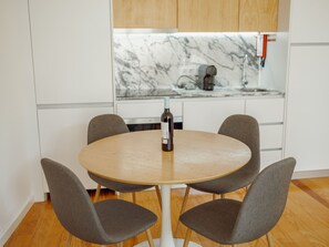 A modern kitchen with white cabinets, a marble countertop, a built-in oven, and a round table with four grey chairs. - Apartment  by Interhome (Porto)