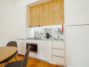 A compact kitchen with white cabinetry, a wooden countertop, a built-in oven, and a marble backsplash. - Apartment  by Interhome (Porto)