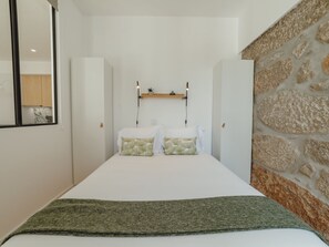 Una camera da letto con un letto, una mensola in legno con oggetti decorativi e un muro in pietra.
