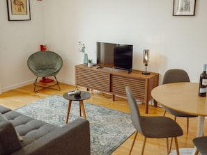 A modern living room with a sofa, a dining table, a TV on a wooden cabinet, and a small side table with a remote control. - Apartment  by Interhome (Porto)