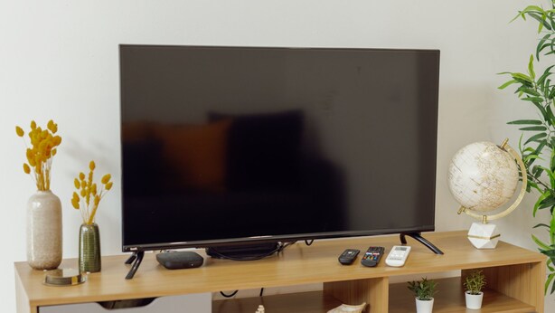 Ein Flachbildfernseher auf einem Holz-TV-Möbel mit Ablagen darunter.