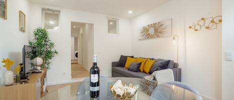 A modern living room with a glass coffee table, a sofa with cushions, a potted plant, and a wine bottle.