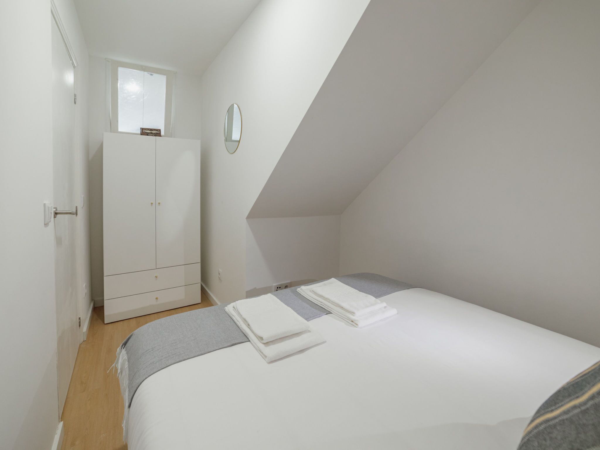 A bedroom with a bed, a wardrobe, a mirror, and a window.
