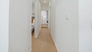 Ein schmaler Flur mit Holzboden, der zu einem Zimmer mit einem Bett und einer Waschmaschine führt.