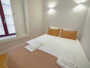 A hotel room with a bed, two pillows, a window with curtains, and a wall-mounted light fixture. - Apartment  by Interhome (Porto)