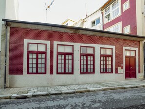 Um edifício com fachada de tijolos vermelhos, várias janelas com molduras brancas e uma porta vermelha.